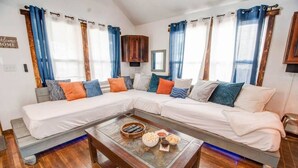 A modern living room with a sectional sofa, a coffee table with snacks, and a 'Welcome Home' sign. - The Breakaway Cottage w/ Steam Room & Loft (+3bd) (Virginia Beach)