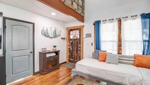 A room with a wooden floor, a bed with white bedding, a fireplace, a window with blue curtains, and a door with a rustic design.
