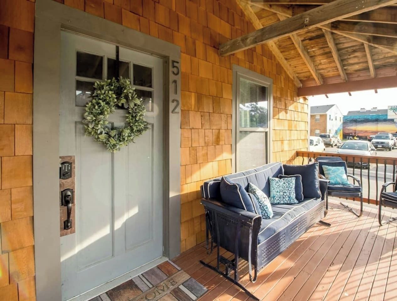 A wooden exterior with a white door, number 512, a wreath, a porch with a blue sofa and chairs, and a street view.