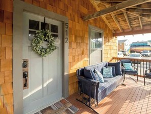 A wooden exterior with a white door, number 512, a wreath, a porch with a blue sofa and chairs, and a street view.