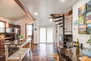 A modern kitchen with a built-in oven, a dining area with a wooden table, and a staircase leading to an upper level.