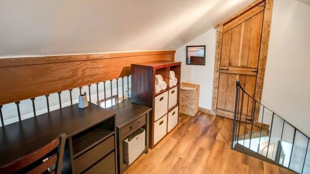 A loft-style room with a wooden desk, storage cabinets, and a staircase leading to an upper level.