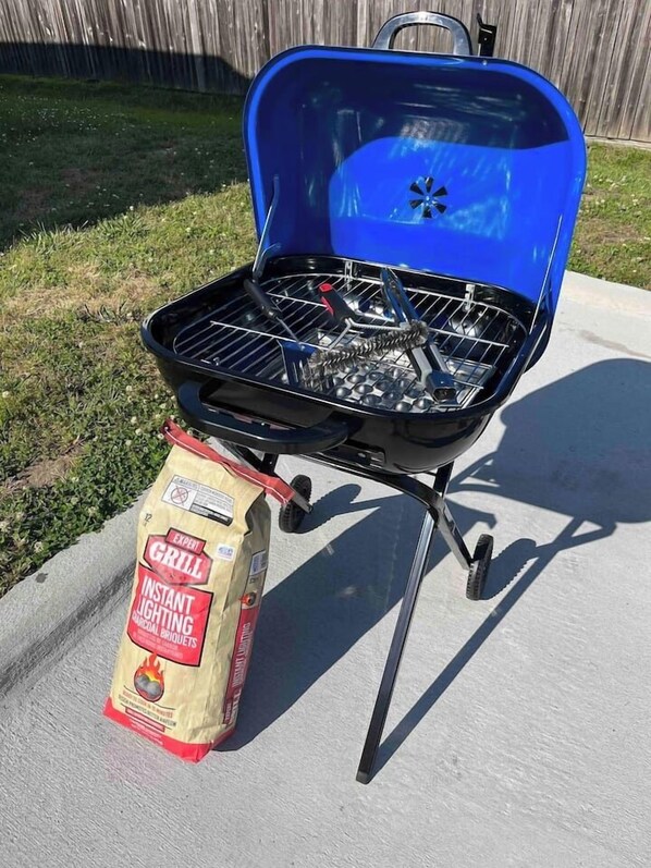 A blue barbecue grill with a bag of instant lighting charcoal briquettes placed in front of it.