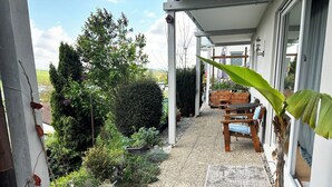 Un portico coperto con una panca in legno, una pianta in vaso e un’area giardino con diverse piante e un piccolo tavolo.