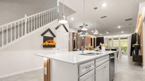 Une cuisine moderne dotée d’un grand îlot central, de luminaires suspendus et d’un escalier avec une rampe.