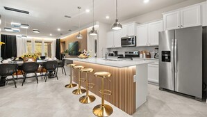 Une cuisine moderne avec des meubles blancs, des appareils en acier inoxydable et un îlot central doté de tabourets de bar.