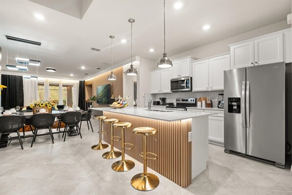 Une cuisine moderne avec des meubles blancs, des appareils en acier inoxydable et un îlot central doté de tabourets de bar.
