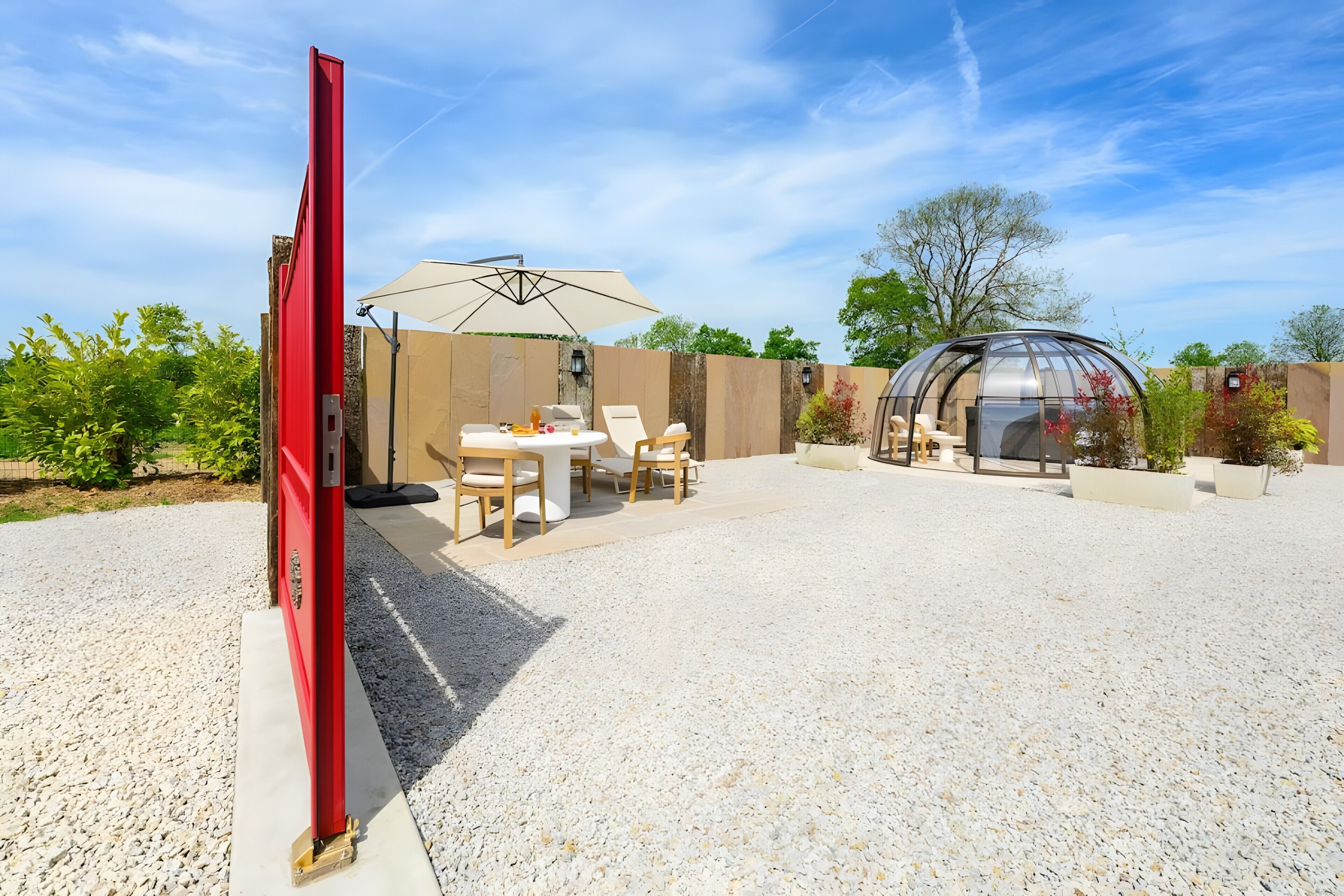 A patio area with a table and chairs, a red structure, and a glass enclosure.