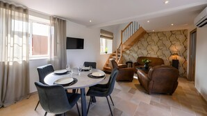 A dining area with a round table, chairs, and a TV mounted on the wall. - Holiday Home 'L'Ascalon' with Private Jacuzzi under Glass Dome, Wi-Fi & Air Conditioning (Saint-Sauveur-le-Vicomte)