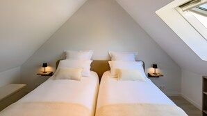 A bedroom with a sloped ceiling, two beds with white bedding, bedside lamps, and a skylight. - Holiday Home 'L'Ascalon' with Private Jacuzzi under Glass Dome, Wi-Fi & Air Conditioning (Saint-Sauveur-le-Vicomte)