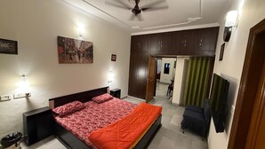 Een slaapkamer met een bed, nachtkastjes, een plafondventilator, een televisie en een deur naar een andere kamer.