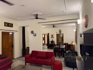 A living room with a red sofa, a ceiling fan, and a dining area with a table and chairs. - Bienvenue Homestay - Charming 2-bedroom house in beautiful Panchkula with AC (Panchkula)