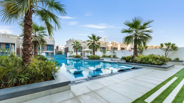 A modern outdoor pool area with palm trees, a clear blue sky, and a well-maintained lawn. - Modern 1 BR Oxford Terraces (Dubai)