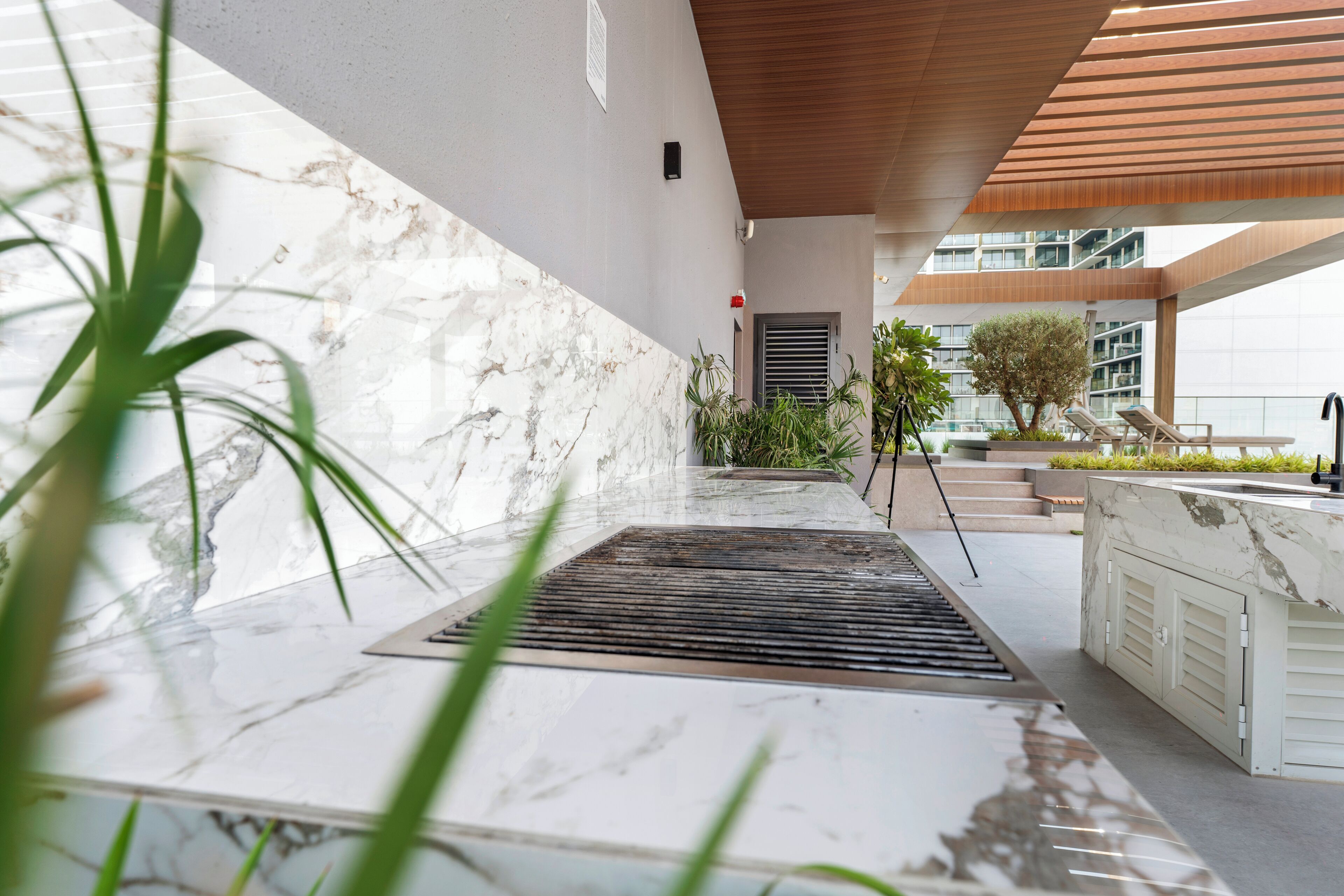 A modern outdoor area with a marble floor, a metal grate, and a wooden ceiling.