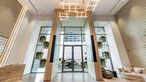 A modern lobby with a glass entrance, wooden accents, and hanging plants. - Modern 1 BR Oxford Terraces (Dubai)