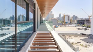 A modern building with a glass balcony, wooden steps, and a view of a construction site with cranes. - Modern 1 BR Oxford Terraces (Dubai)