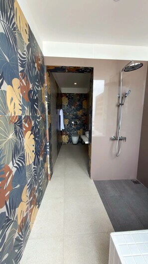 Un baño moderno con ducha, inodoro y lavamanos. Las paredes están decoradas con un estampado de hojas tropicales.
