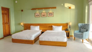 A hotel room with two wooden beds, a chair, a bedside table with a phone, and wall-mounted pictures.