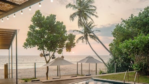 A swimming pool with a view of the sea, surrounded by palm trees and umbrellas.