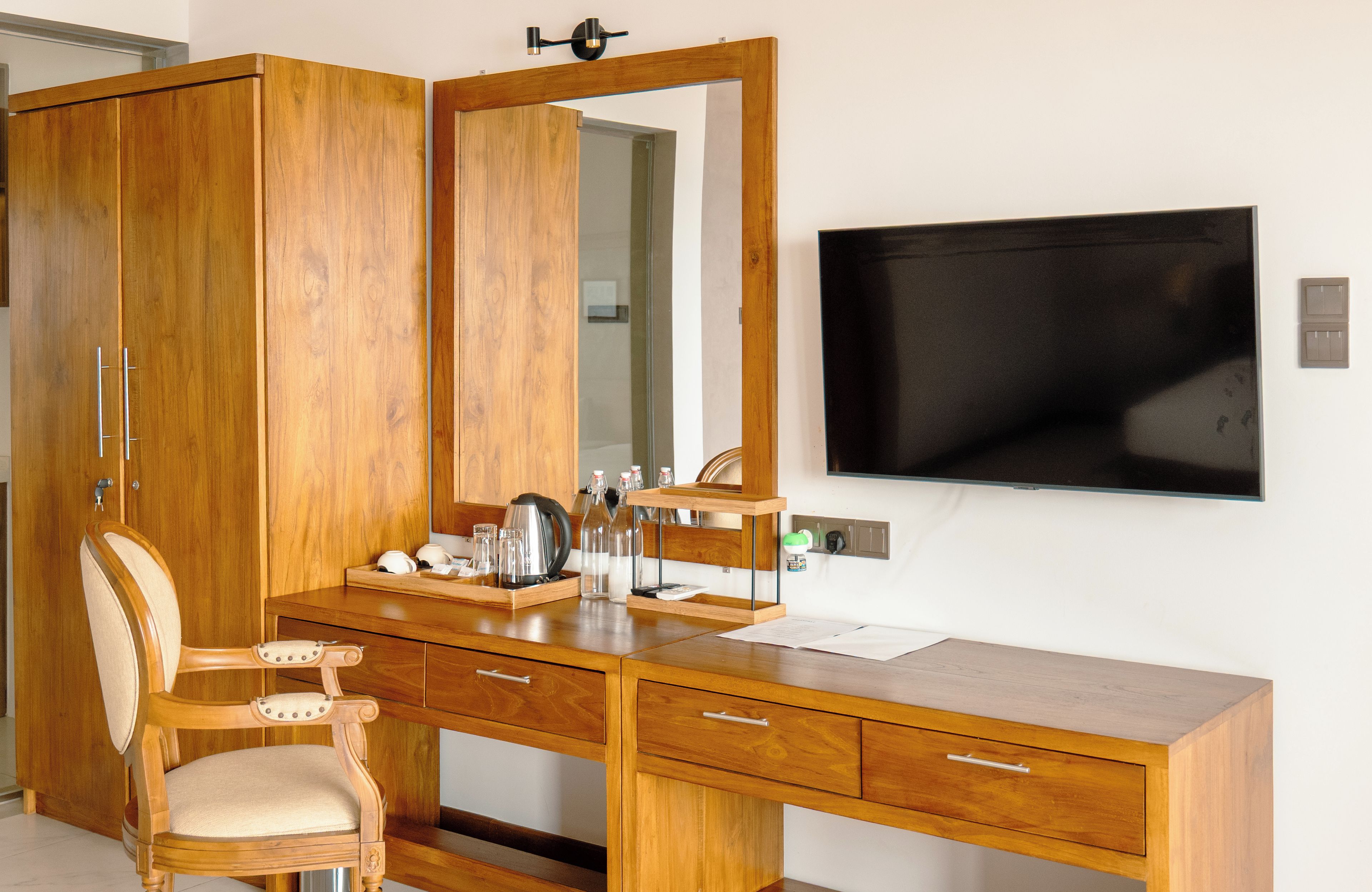 Un bureau en bois avec un miroir, une chaise et un téléviseur fixé au mur.
