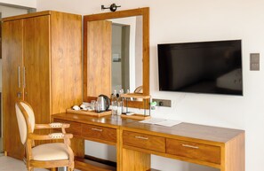 Een houten bureau met een spiegel, een stoel en een televisie aan de wand.