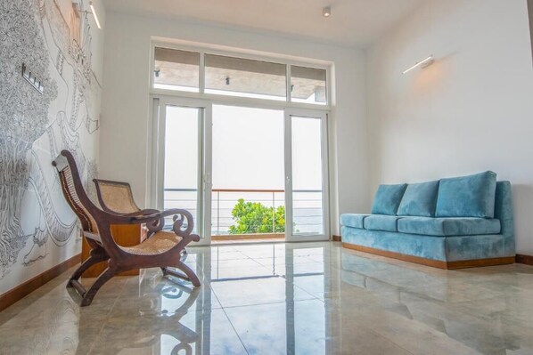 Una habitación amplia con un gran ventanal corredero que da a un balcón, un sofá azul y una silla de madera.