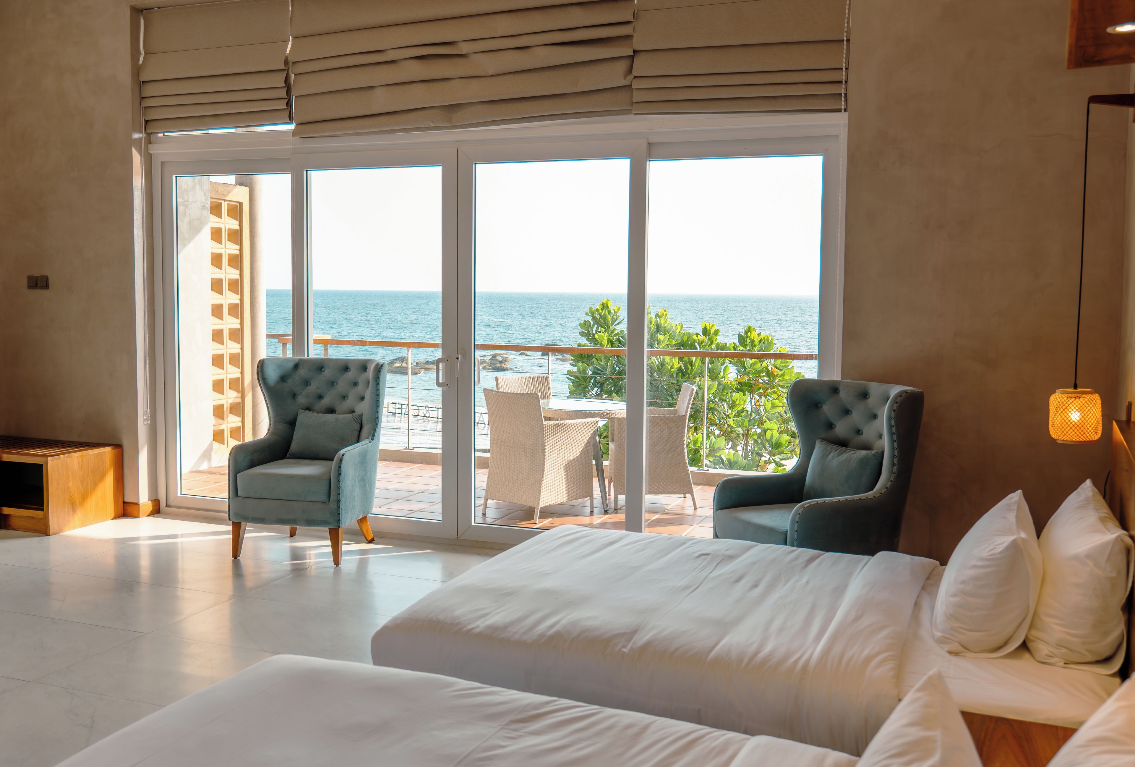 A hotel room with a large bed, two armchairs, a view of the sea, and a balcony with outdoor furniture.