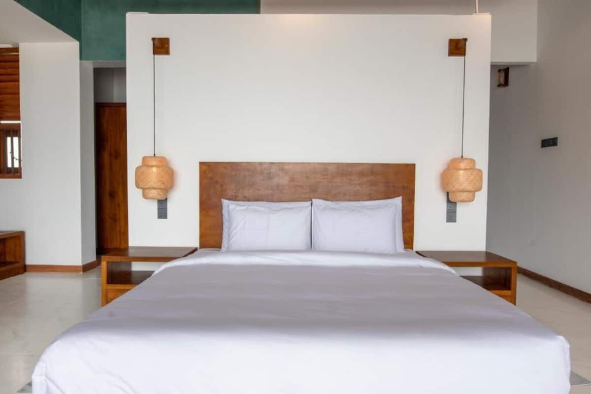 A neatly made bed with white linens, a wooden headboard, and two wall-mounted lamps.
