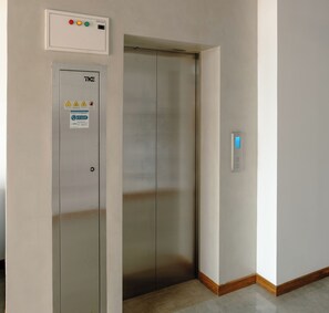Un ascenseur doté d’un panneau de commande situé au-dessus de la porte, d’un panneau d’avertissement de sécurité et d’un écran numérique fixé au mur.