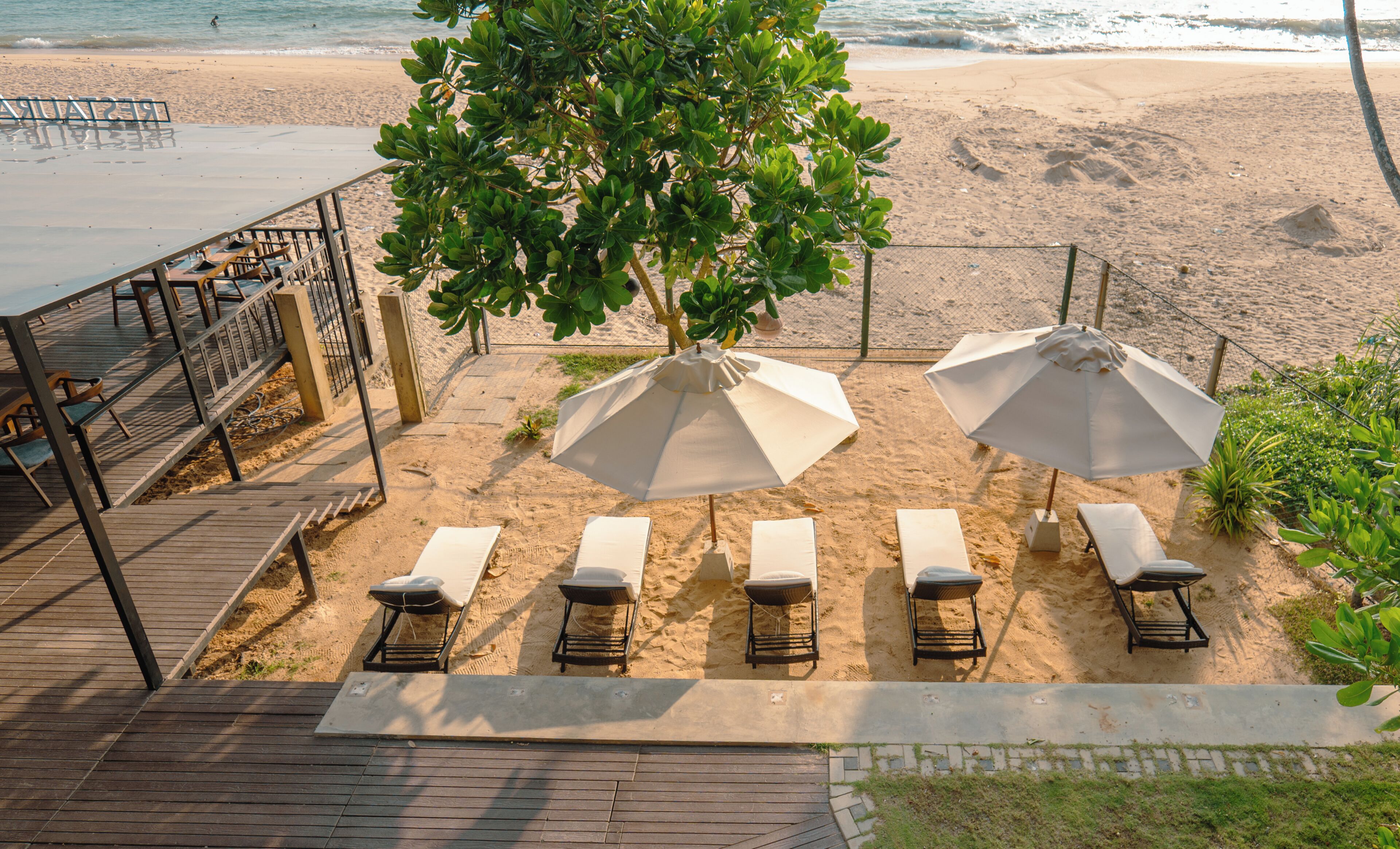 Eine Strandlounge mit Liegestühlen und Sonnenschirmen, ein Holzdeck und Blick aufs Meer.
