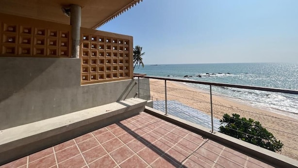 Ein Balkon mit Fliesenboden, Blick auf den Strand und ein Gebäude mit einer gemusterten Fassade.