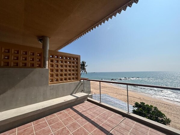 Un balcón con suelo de baldosas, vista a la playa y un edificio con fachada decorada.