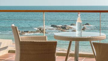 Een ronde tafel met twee rieten stoelen op een terras met uitzicht op zee, met een fles op de tafel.