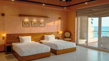 Une chambre d’hôtel avec deux lits, une tête de lit en bois, une grande fenêtre donnant sur la mer et un luminaire fixé au mur.