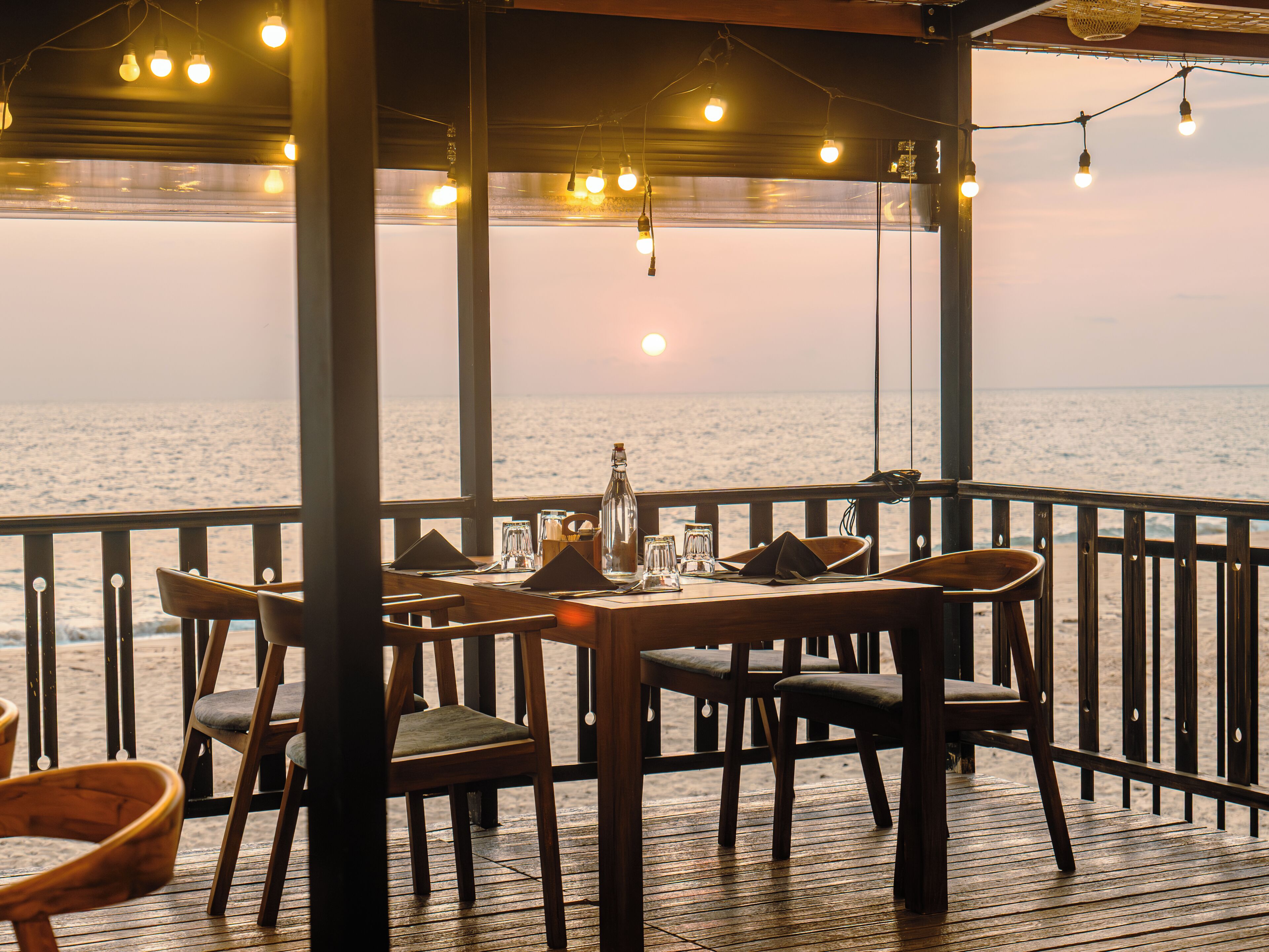 A wooden deck with a table set for dining, overlooking a body of water.