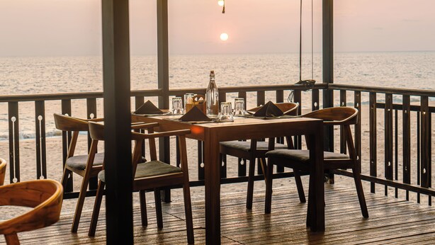 A wooden deck with a table set for dining, overlooking a body of water.
