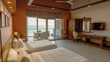 A hotel room with two beds, a desk, a television, and a view of the sea.