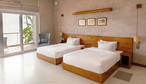 A hotel room with two beds, a chair, a balcony, and a wall-mounted shelf with pictures. - At Kelly's Ambalangoda (Ambalangoda)