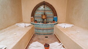 A small, private bathroom with a tiled floor, a central basin, and two towel-wrapped benches. - Riad le Graff Pink (Marrakech)