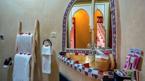 A bathroom with a large mirror, a sink with a gold basin, and towels hanging on the wall. - Riad le Graff Pink (Marrakech)