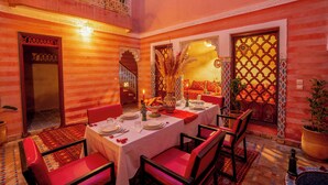 A dining area with a table set for four, surrounded by red chairs, in a room with ornate walls and a balcony. - Riad le Graff Pink (Marrakech)