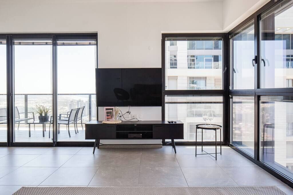 Un soggiorno moderno con una grande TV a schermo piatto, un mobile intrattenimento nero e un tavolino con un bicchiere di vino.