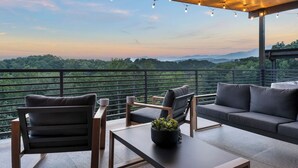 A balcony with a view of a forested landscape, furnished with a sofa, chairs, and a table. - Rooftop Hot Tub, Indoor Pool, Sunrise & Mtn Views (Pigeon Forge)