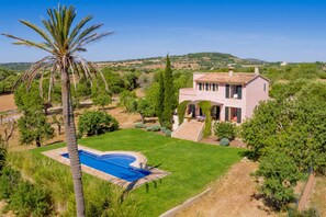 A house with a swimming pool, surrounded by greenery and hills.
