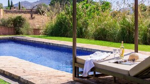 Ein Pool mit Holzterrasse, eine Liege mit Handtuch, eine Flasche und ein Strohhut.