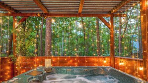 Un bain à remous avec une terrasse en bois et vue sur une forêt.