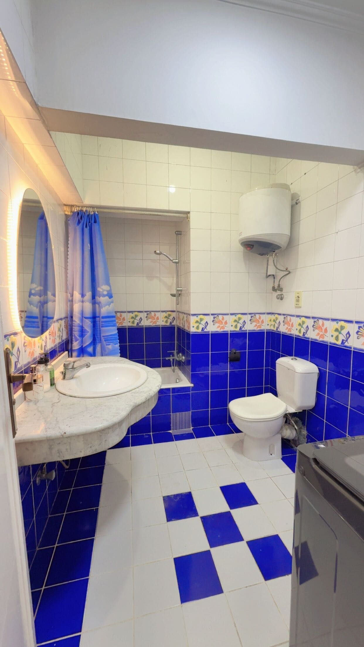 A bathroom with a white sink, blue and white tiled floor, a toilet, and a shower.