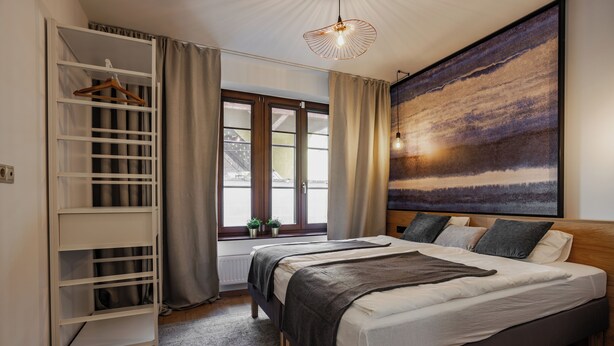Un dormitorio con cama, armario, ventana con cortinas y un cuadro en la pared.