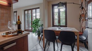 Una cocina moderna con comedor, que cuenta con un amplio ventanal, una planta en maceta y una botella de vino en la encimera.