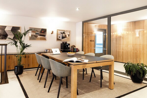A modern meeting room with a wooden table, grey chairs, a laptop, a coffee machine, and books. - Native Waterloo (London)